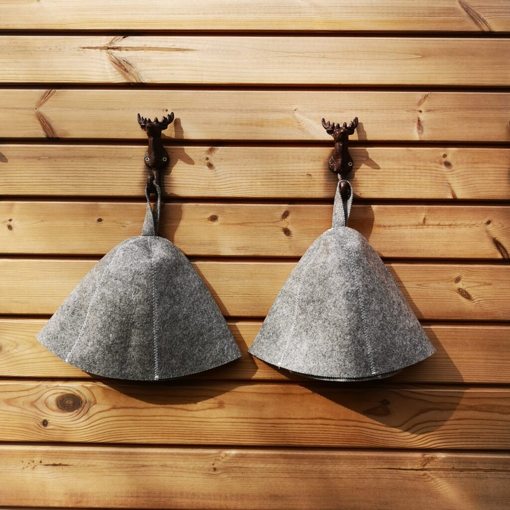 Two sauna hats hanging on hooks inside wooden sauna.